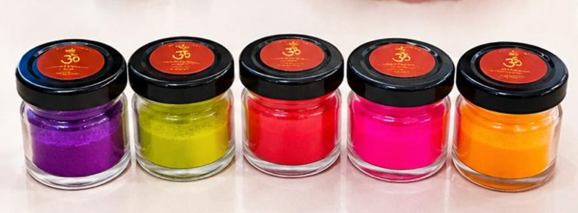 Purple, yellow-green, red, pink and orange jar candles with black lids and Om labels.